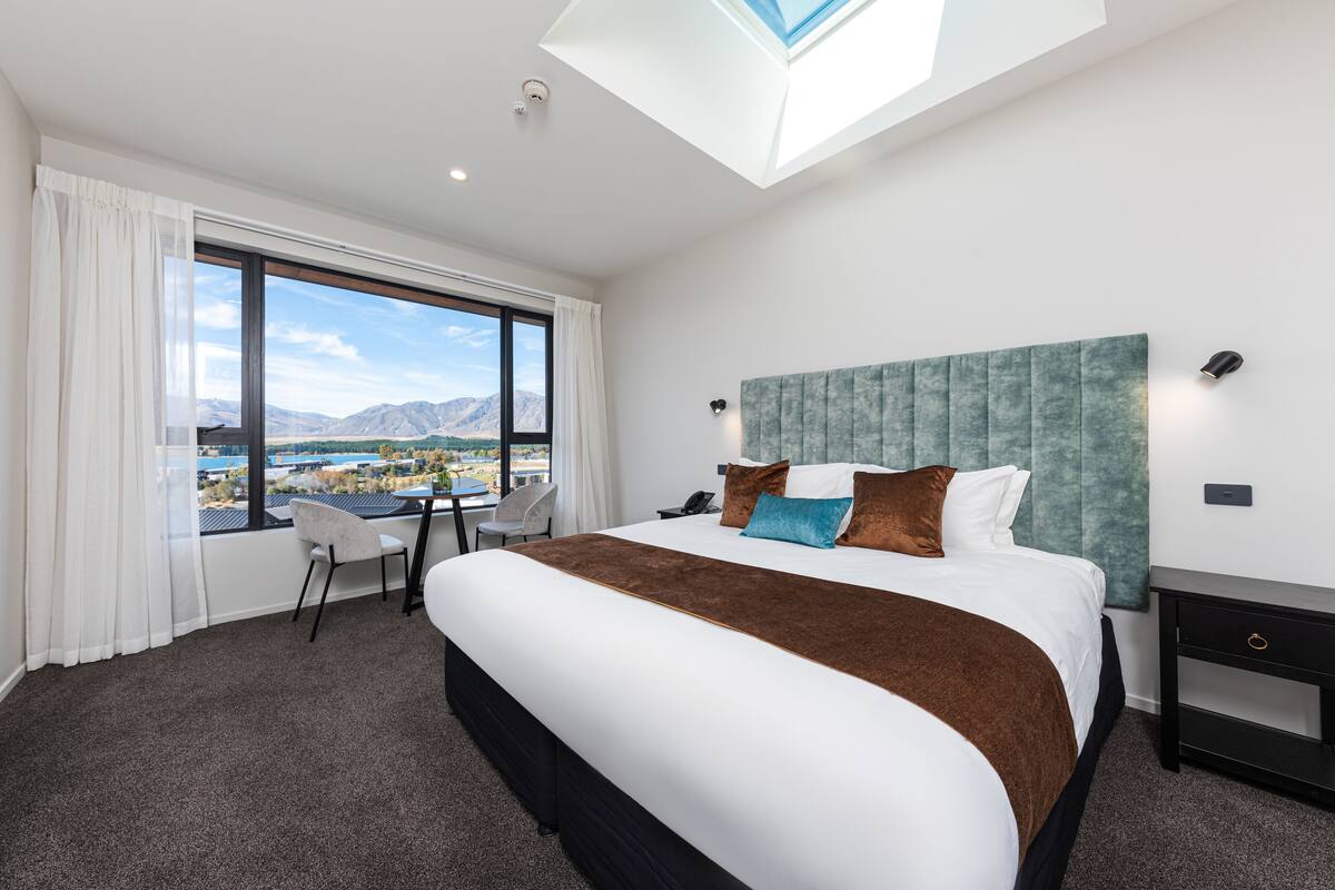 Habitación de hotel moderna con una cama grande, un escritorio y vistas a un paisaje montañoso a través de un ventanal.