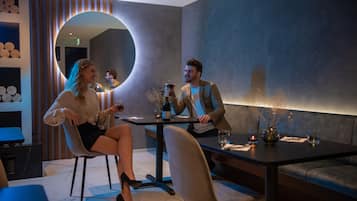A modern dining area with a round mirror, a table with two chairs, and a vase with flowers.