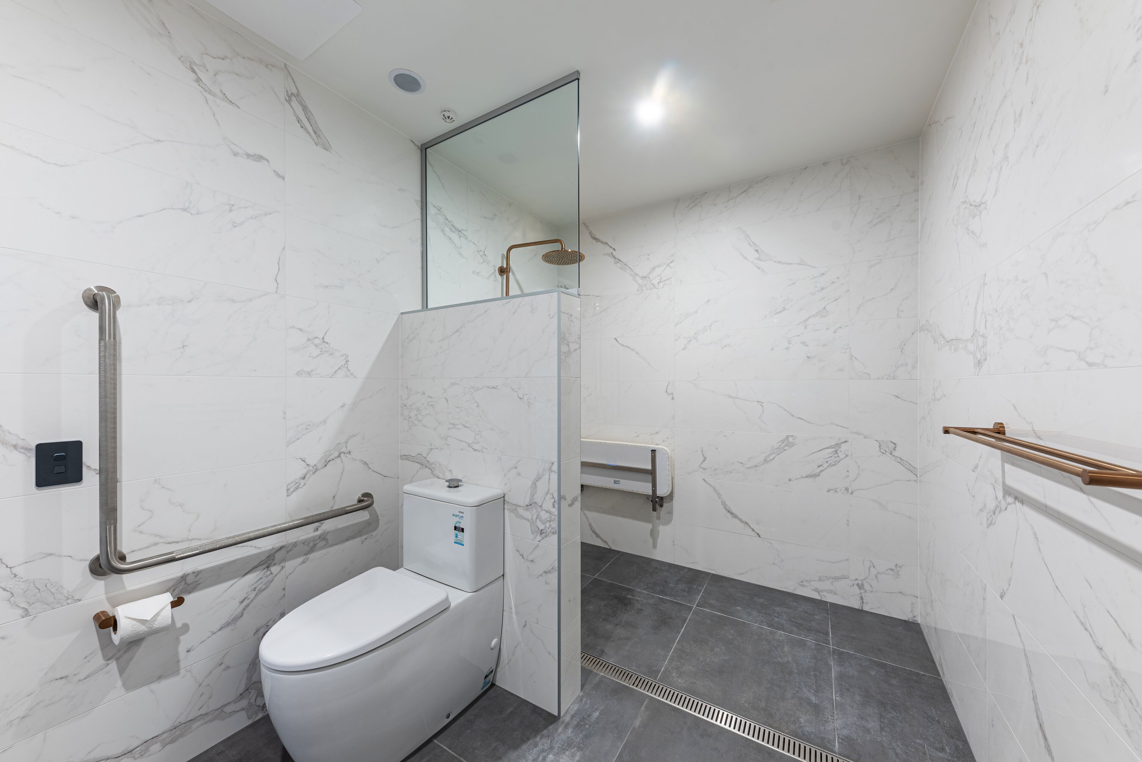 A modern bathroom with a toilet, a shower with a glass door, and a handrail.