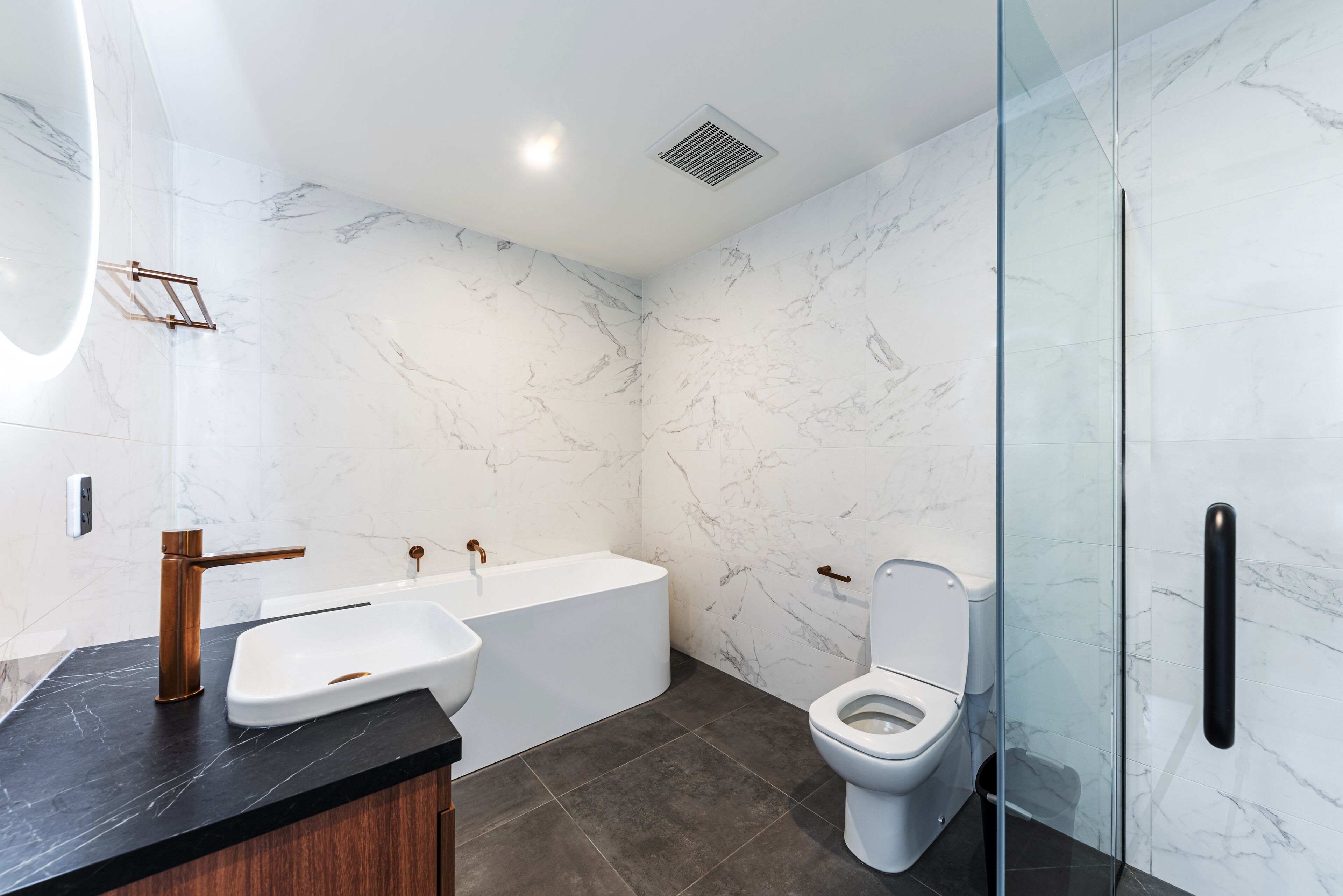A modern bathroom with a marble wall, a bathtub, a sink, and a toilet.