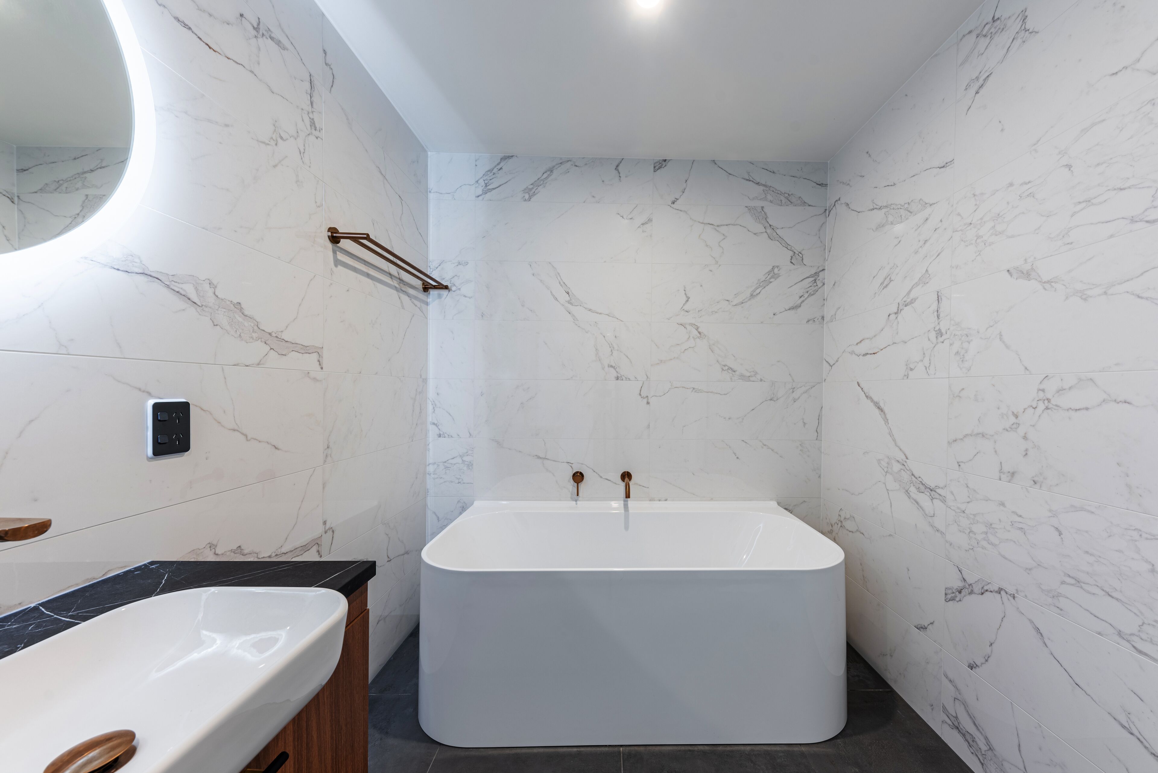 Une salle de bain moderne avec une baignoire sur pieds, un grand miroir et des murs en marbre.