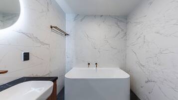 Un baño moderno con una bañera independiente, un espejo grande y paredes de mármol.