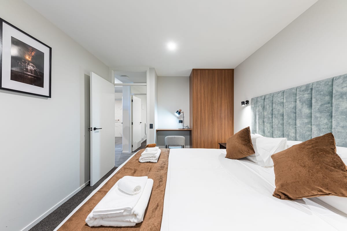 Una habitación de hotel con cama, escritorio, silla y baño visible a través de una puerta abierta.