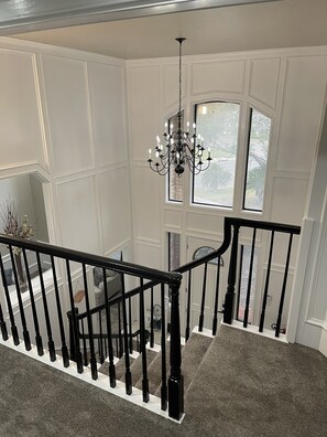 Eine Treppe mit schwarzem Geländer, einer Kristallleuchter und Blick durch ein Fenster nach draußen.