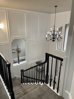 A staircase with a black railing, a chandelier, and a window with a vase of flowers. - Breathtaking, Lakefront, Pool, Private, big group, birds viewing (Harlingen)
