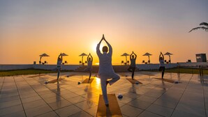Un grupo de personas practicando yoga en un patio con baldosas, con el atardecer de fondo.