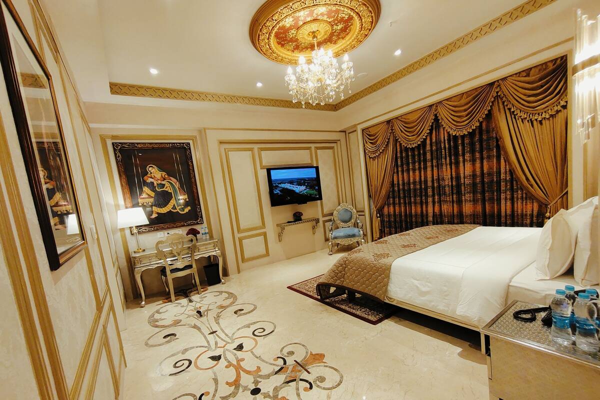 A luxurious hotel room with a large bed, a television, a desk with a chair, and a decorative floor pattern.