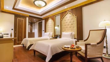 Une chambre d’hôtel avec deux lits, un coin salon comprenant un fauteuil, une petite table ronde et une lampe.