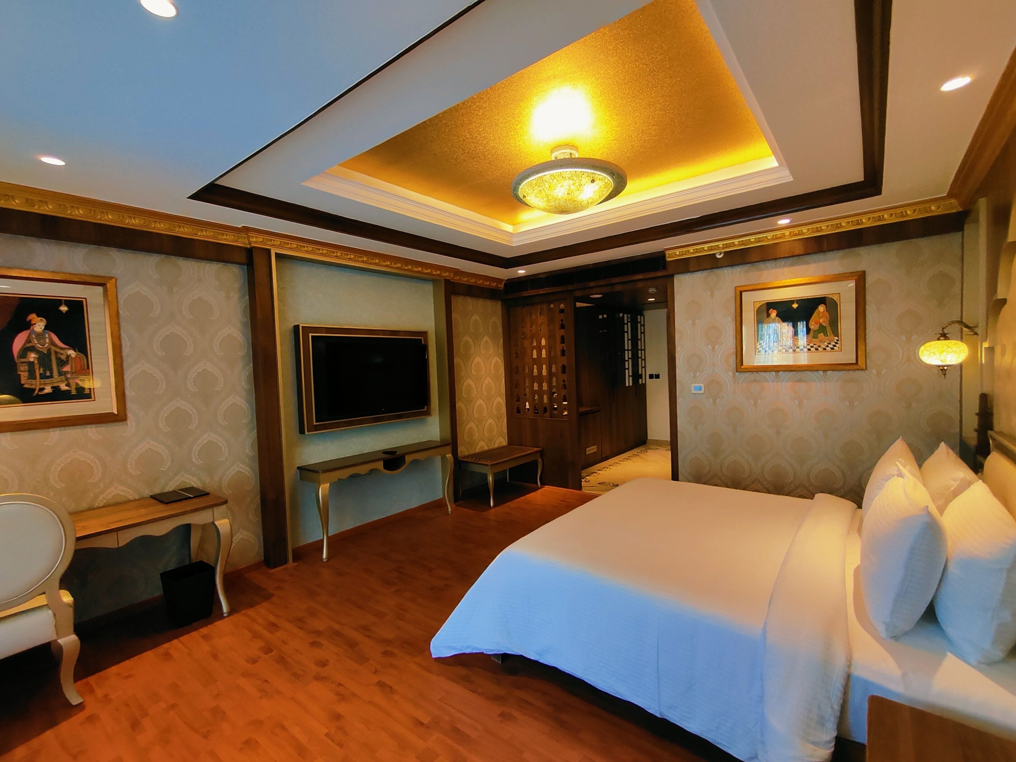 Ein Hotelzimmer mit einem großen Bett, einem Schreibtisch, einem Flachbildfernseher, einem Sessel und Holzboden.