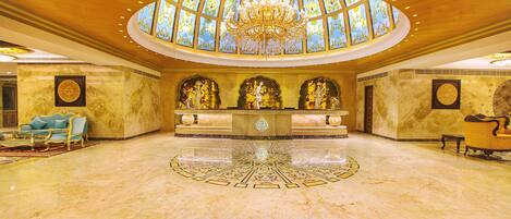 A grand lobby with a central chandelier, a reception desk, and a seating area with sofas.