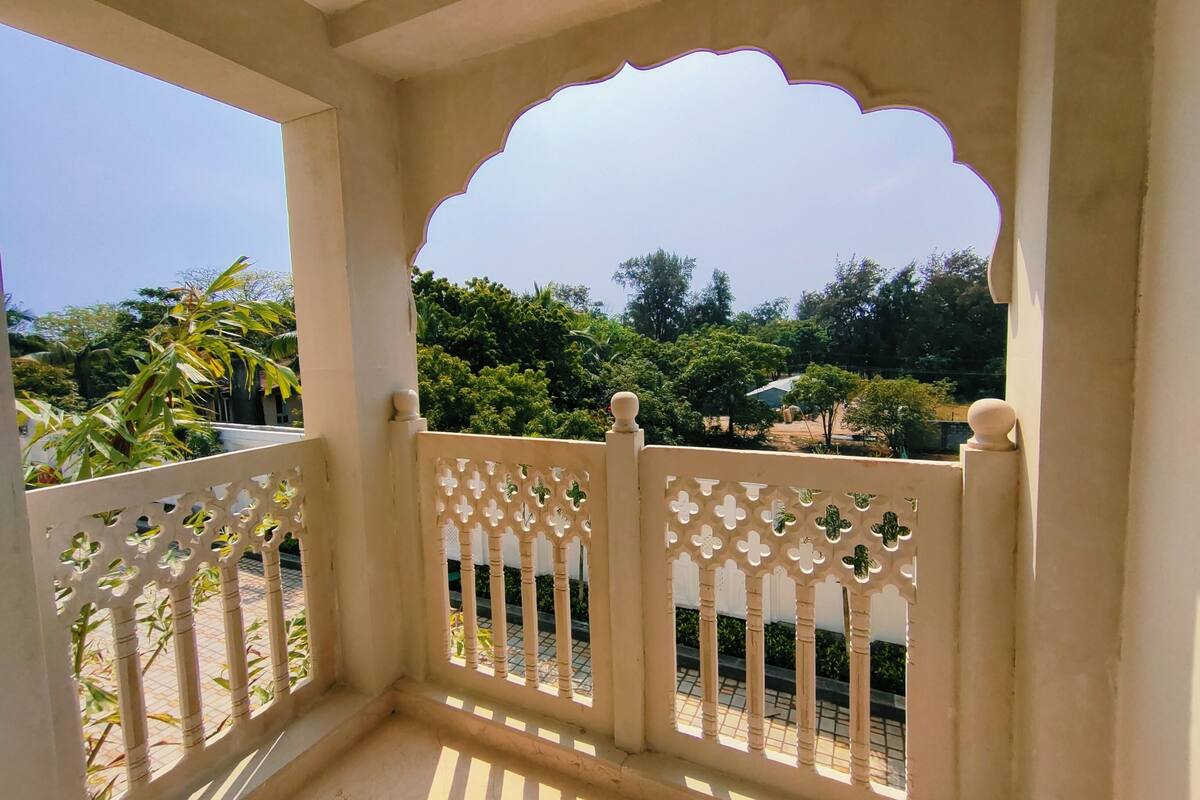 A balcony with a decorative white railing and an archway, overlooking a garden with various plants and trees.