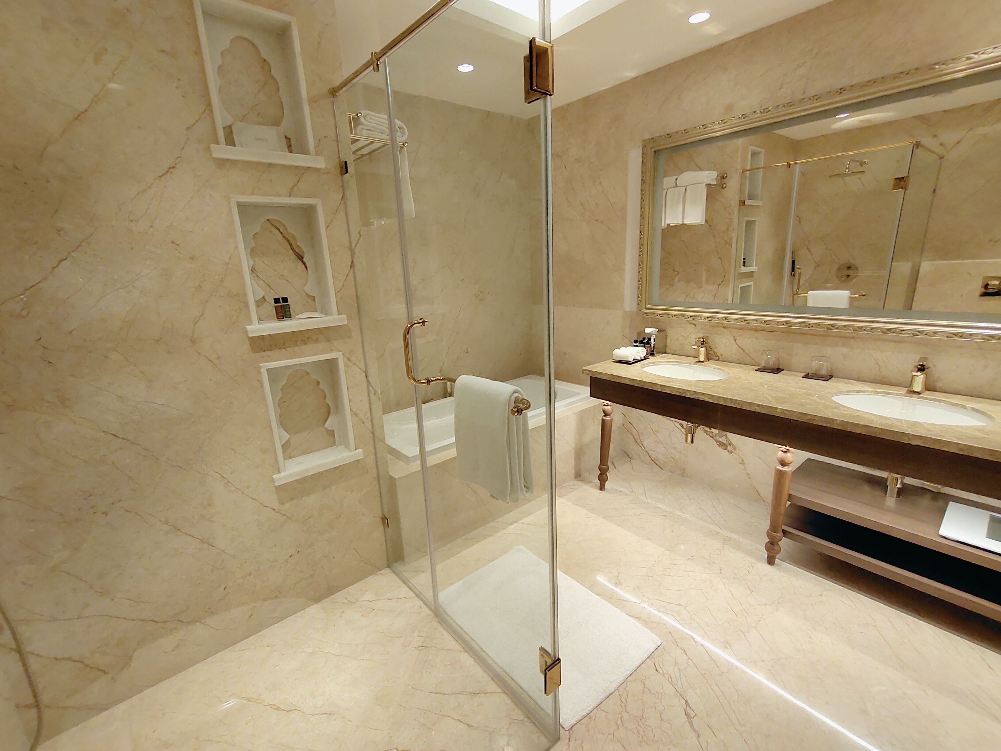 A modern bathroom with a glass-enclosed shower, marble walls, and a large mirror.