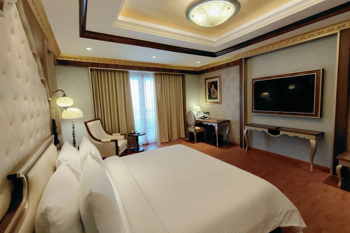 A hotel room with a large bed, a desk with a chair, a television, and a window with curtains.