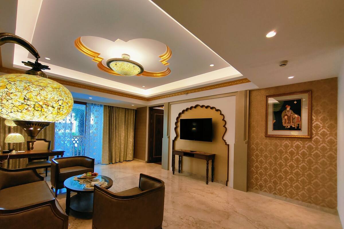 A spacious room with a large chandelier, a television mounted on the wall, and a framed picture.
