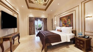 Una habitación de hotel amplia con una cama grande, televisión, candelabro y un cuadro en la pared.