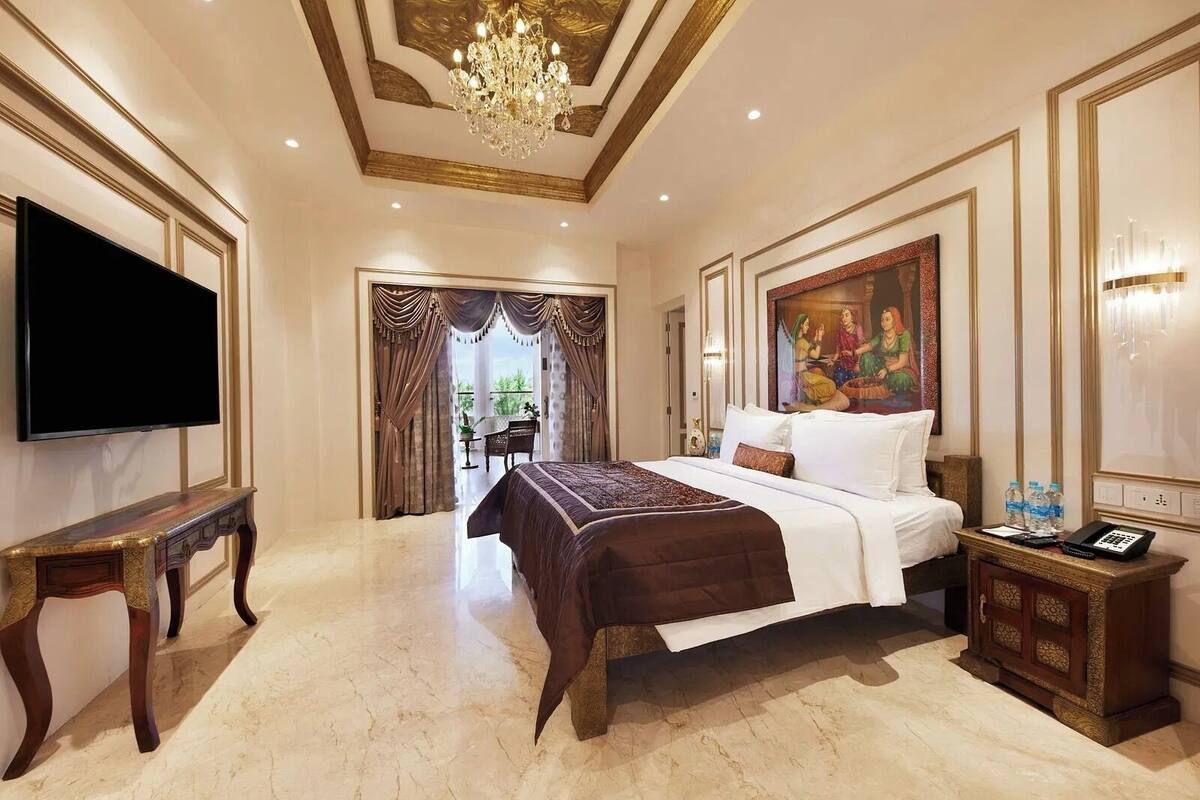 A spacious hotel room with a large bed, a television, a chandelier, and a painting on the wall.