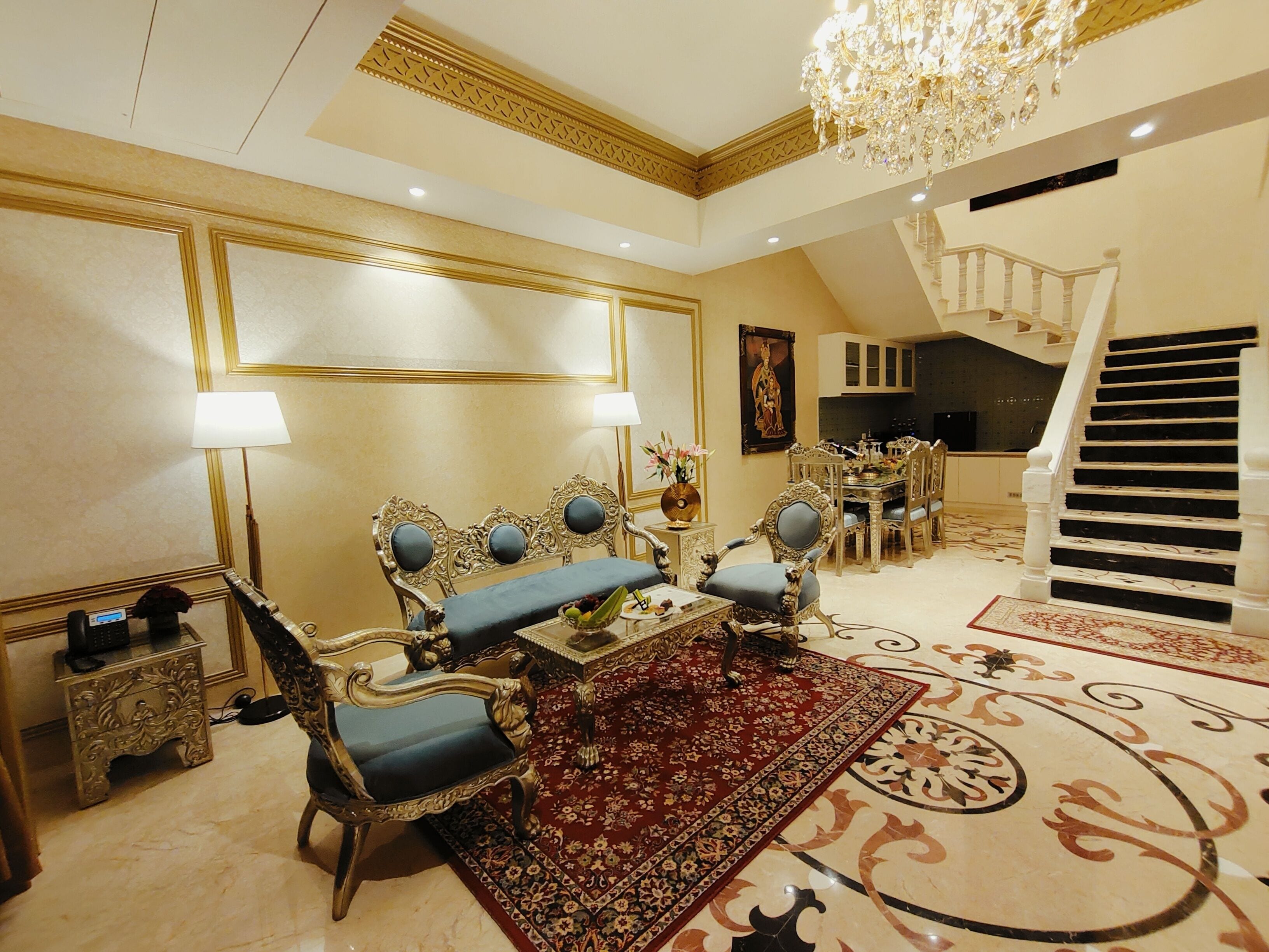 Un amplio salón con muebles ornamentados, un candelabro y una escalera.