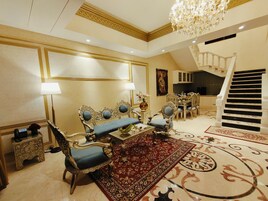 Un amplio salón con muebles ornamentados, un candelabro y una escalera.