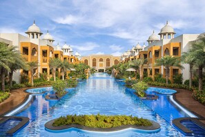 Un área de piscina con varias piscinas, palmeras y un edificio con estructuras abovedadas.
