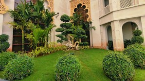 Un patio con abundante vegetación, incluyendo palmeras y arbustos cuidadosamente podados, rodeado de detalles arquitectónicos ornamentales.