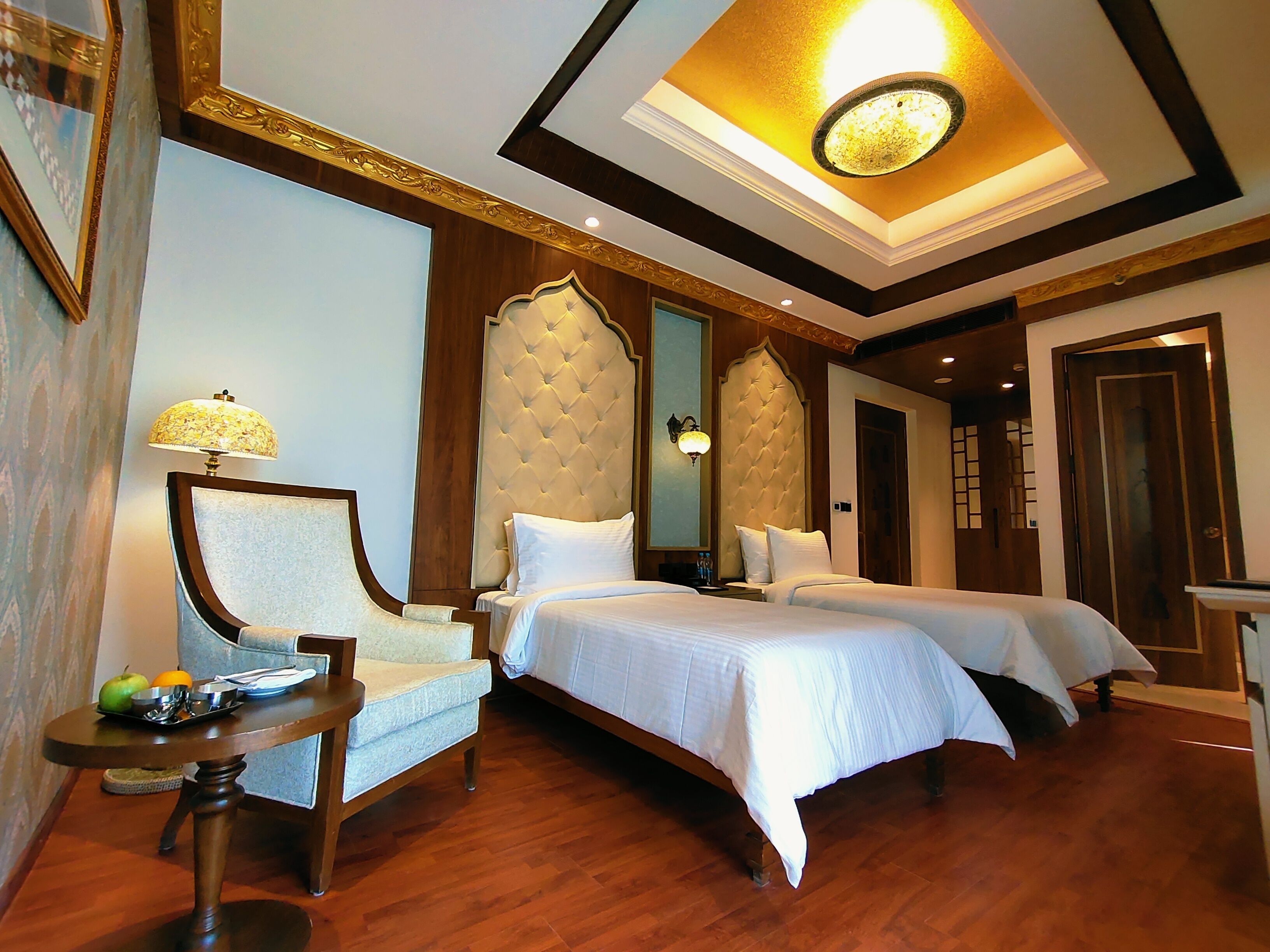 A hotel room with two beds, a sitting area with a chair, a small table, and a ceiling light fixture.