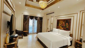 A spacious bedroom with a large bed, a television, a desk, and a painting on the wall.