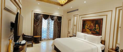 A spacious bedroom with a large bed, a television, a desk, and a painting on the wall.