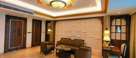 Un hall de hotel con suelo de mármol, un conjunto de sofás, una mesa de comedor con sillas y un techo decorativo.
