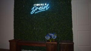 A wall with a neon sign that reads "IT WAS ALL A Dream" and a wooden bench with a vase of flowers. - Dreamville (Maxwell)