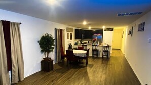 A spacious living area with a dining table and chairs, a potted plant, and a kitchen in the background. - Dreamville (Maxwell)
