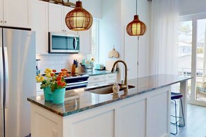 A modern kitchen with white cabinets, a stainless steel refrigerator, a microwave, a sink with a faucet, and two hanging wicker pendant lights.
