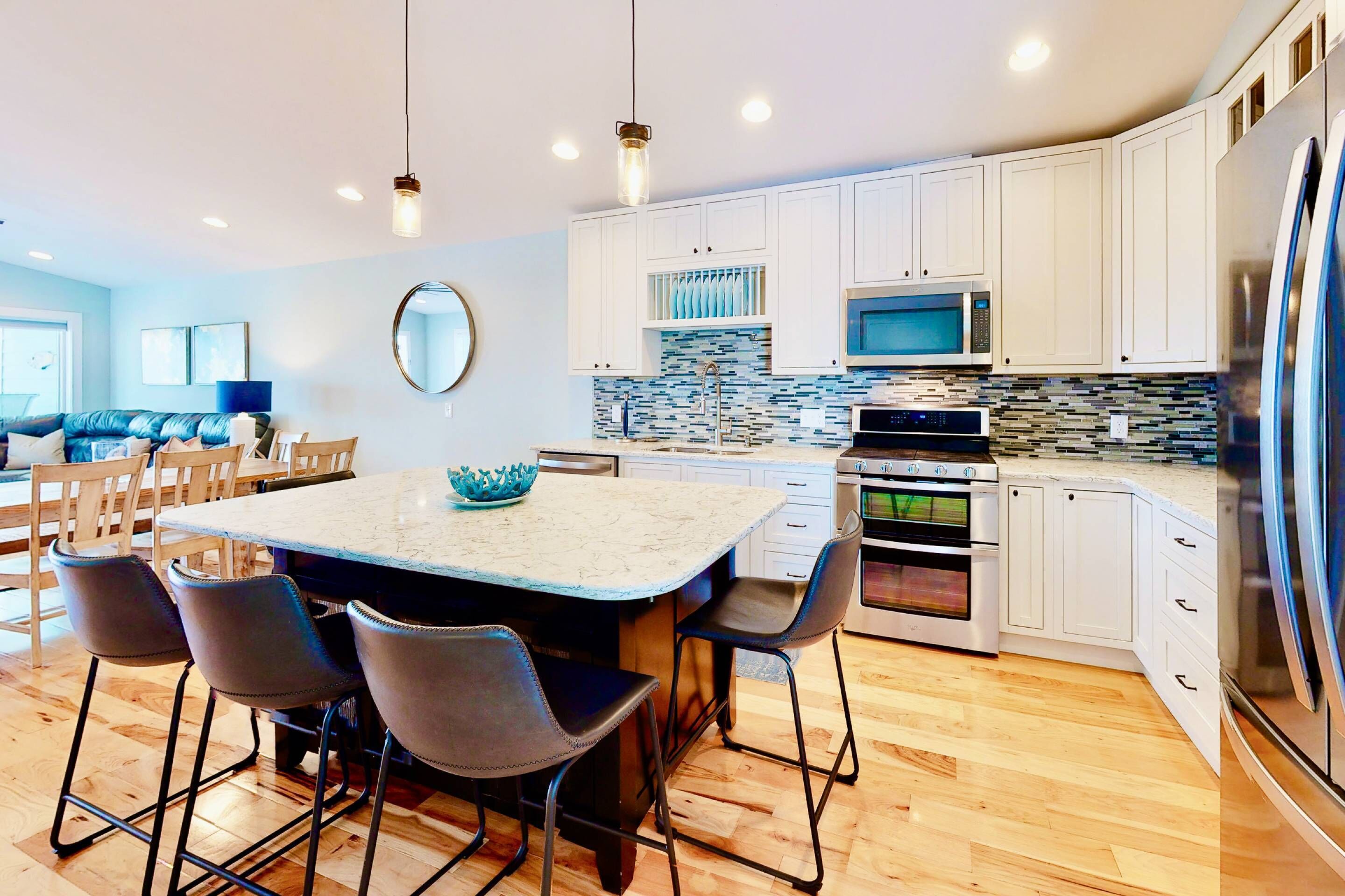 A modern kitchen with white cabinets, a large island with bar stools, a microwave, oven, and a refrigerator.