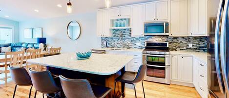 A modern kitchen with white cabinets, a large island with bar stools, a microwave, oven, and a refrigerator.