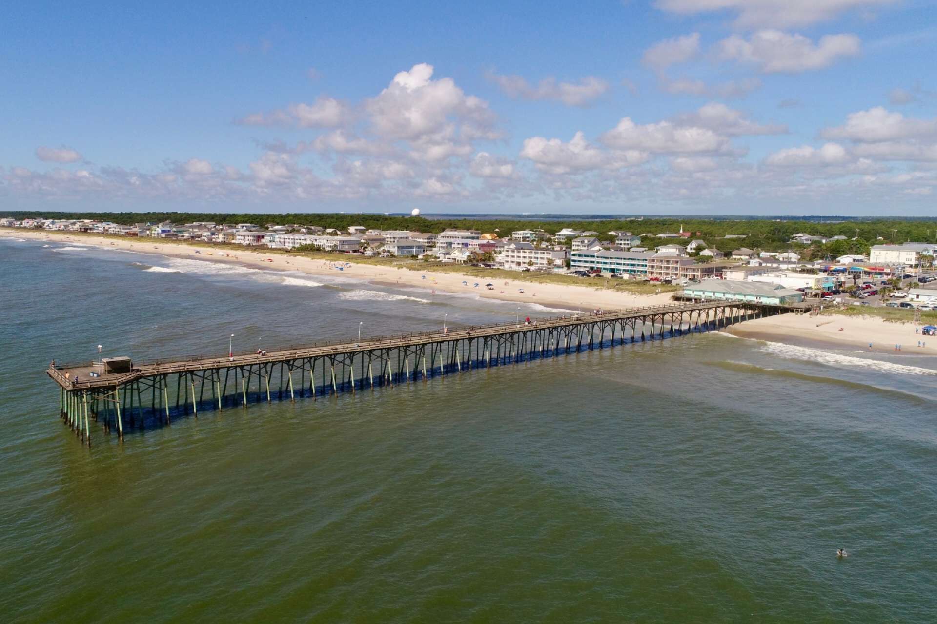 A pier extending into the ocean with a beach and buildings in the background.