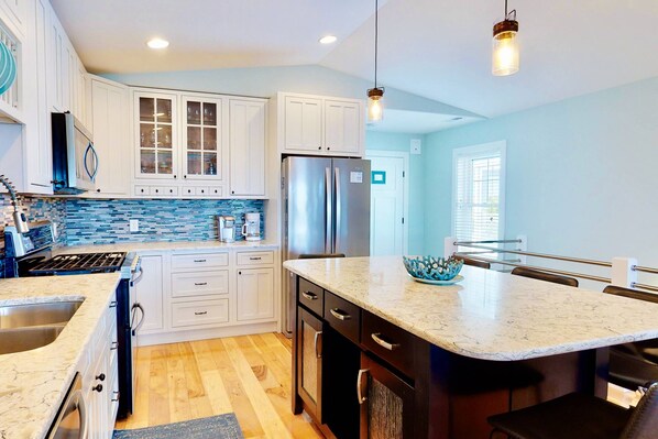 A modern kitchen with white cabinets, a stainless steel refrigerator, and a marble countertop.