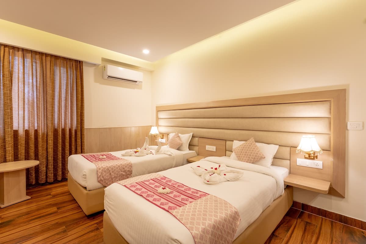 A hotel room with two beds, a bedside table, an air conditioning unit, and a wall-mounted lamp.