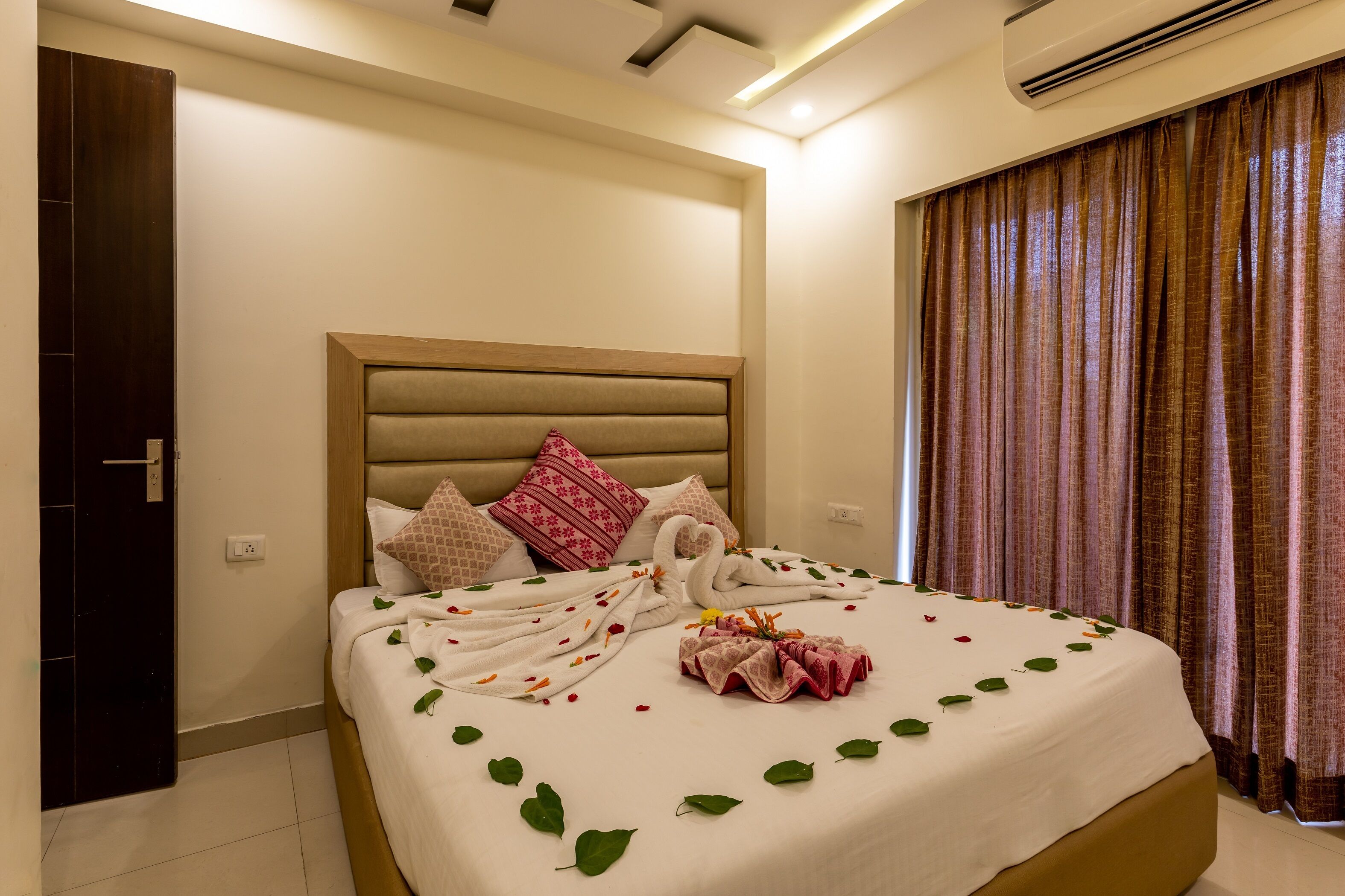 A neatly made bed with a swan towel arrangement, a decorative pillow, and a bouquet of flowers.