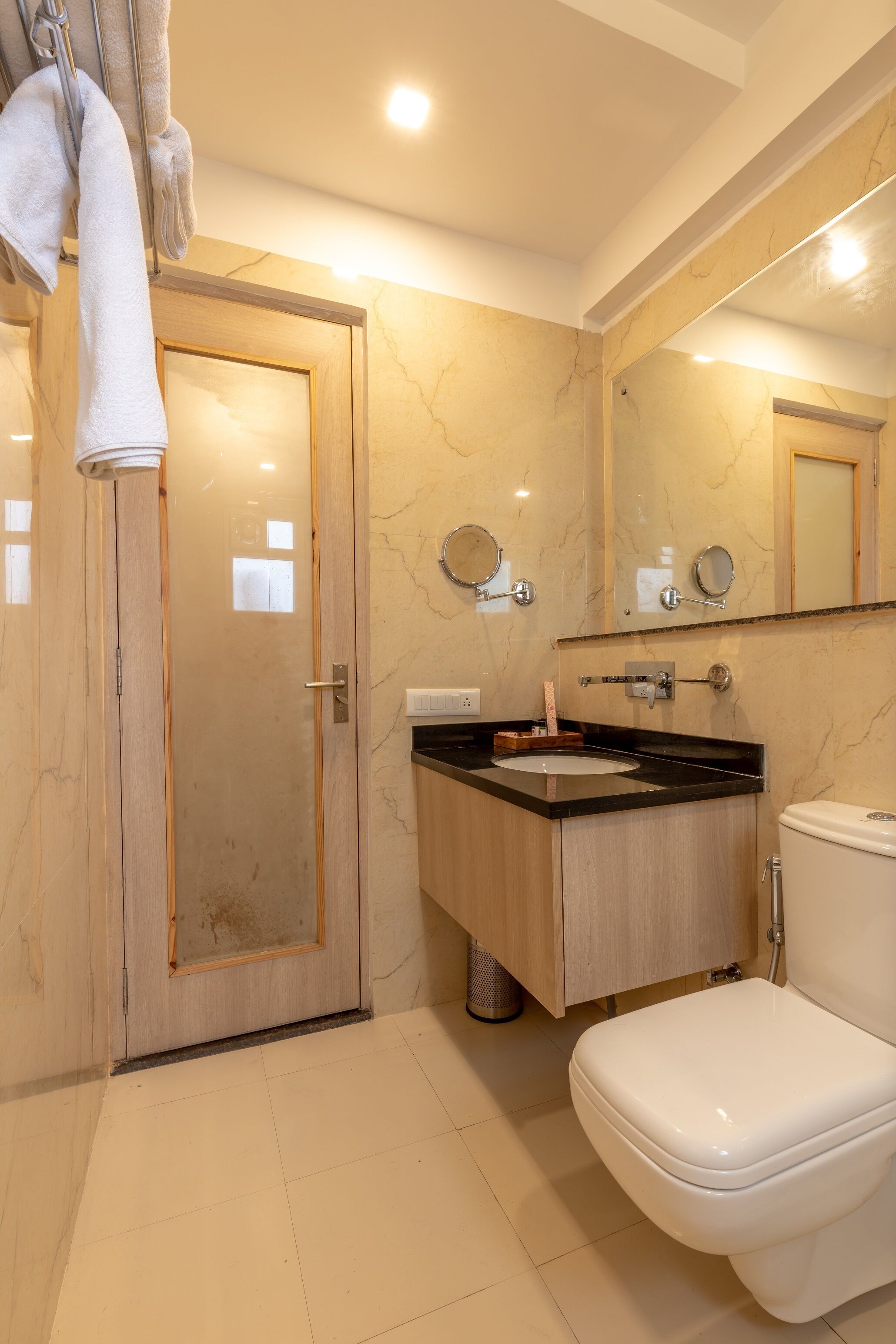 A modern bathroom with a wooden door, a sink with a marble countertop, and a toilet.