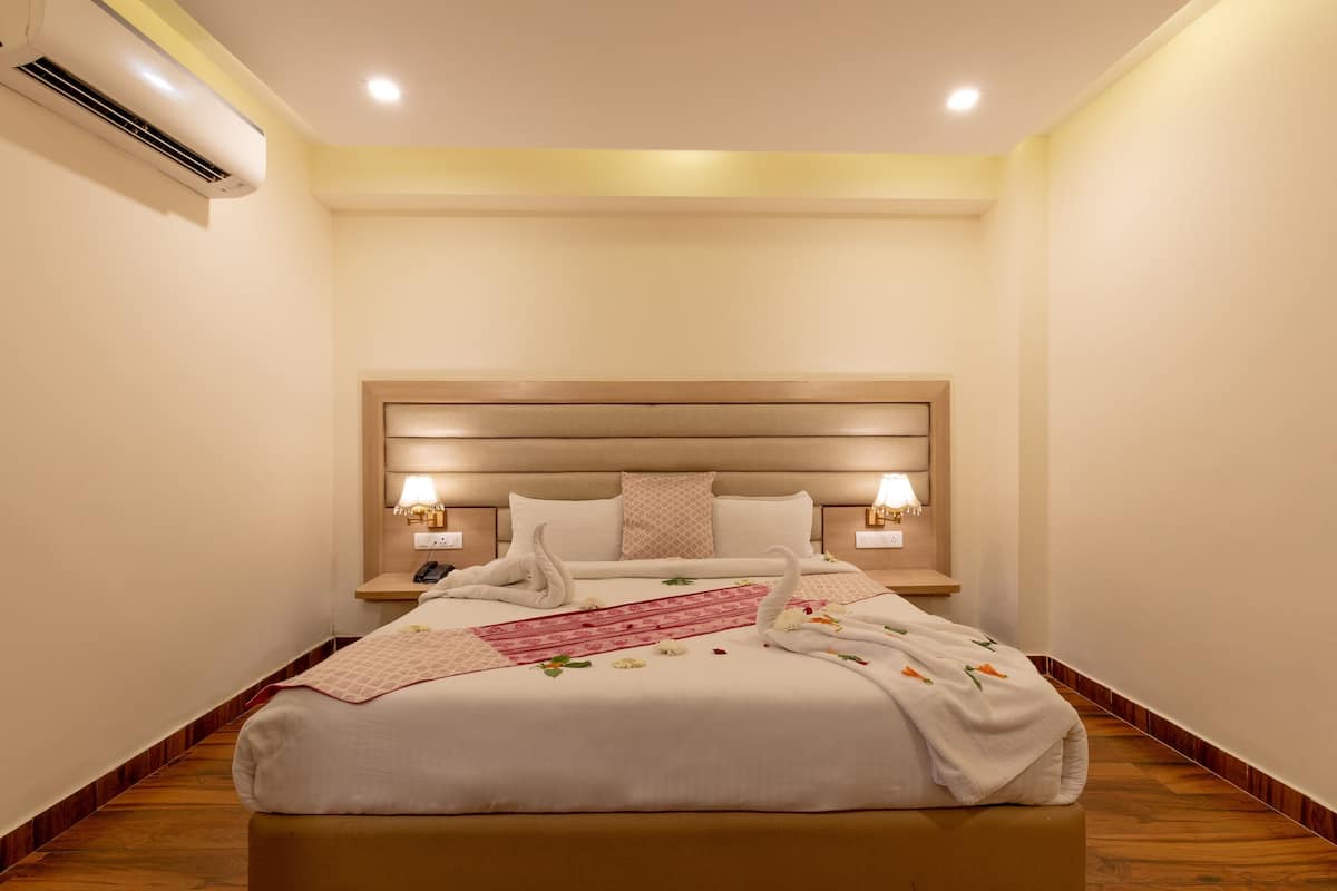 A hotel room with a large bed, bedside lamps, a nightstand, and an air conditioning unit.