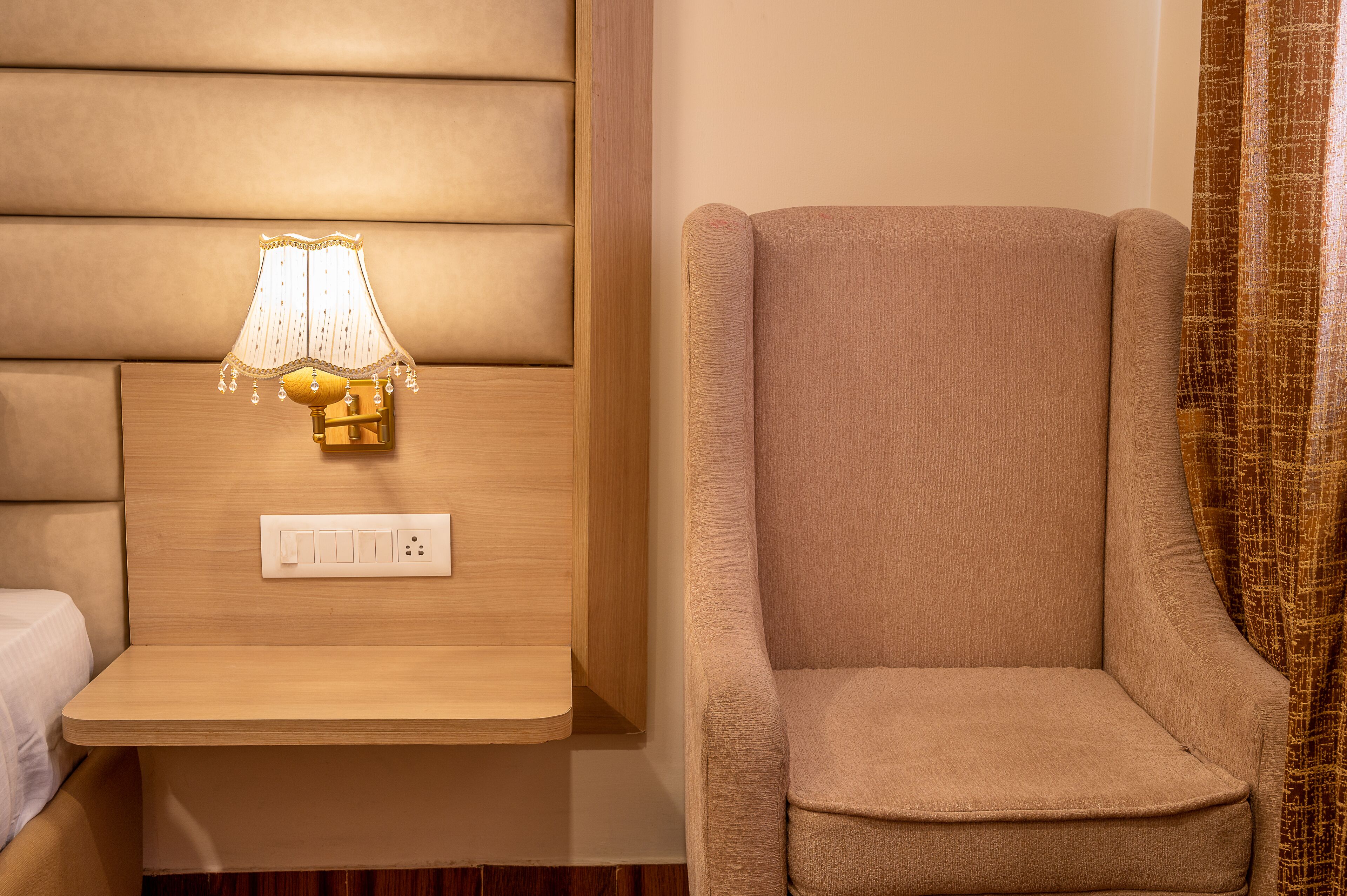 A room with a wooden headboard, a bedside table with a lamp, and a beige armchair.