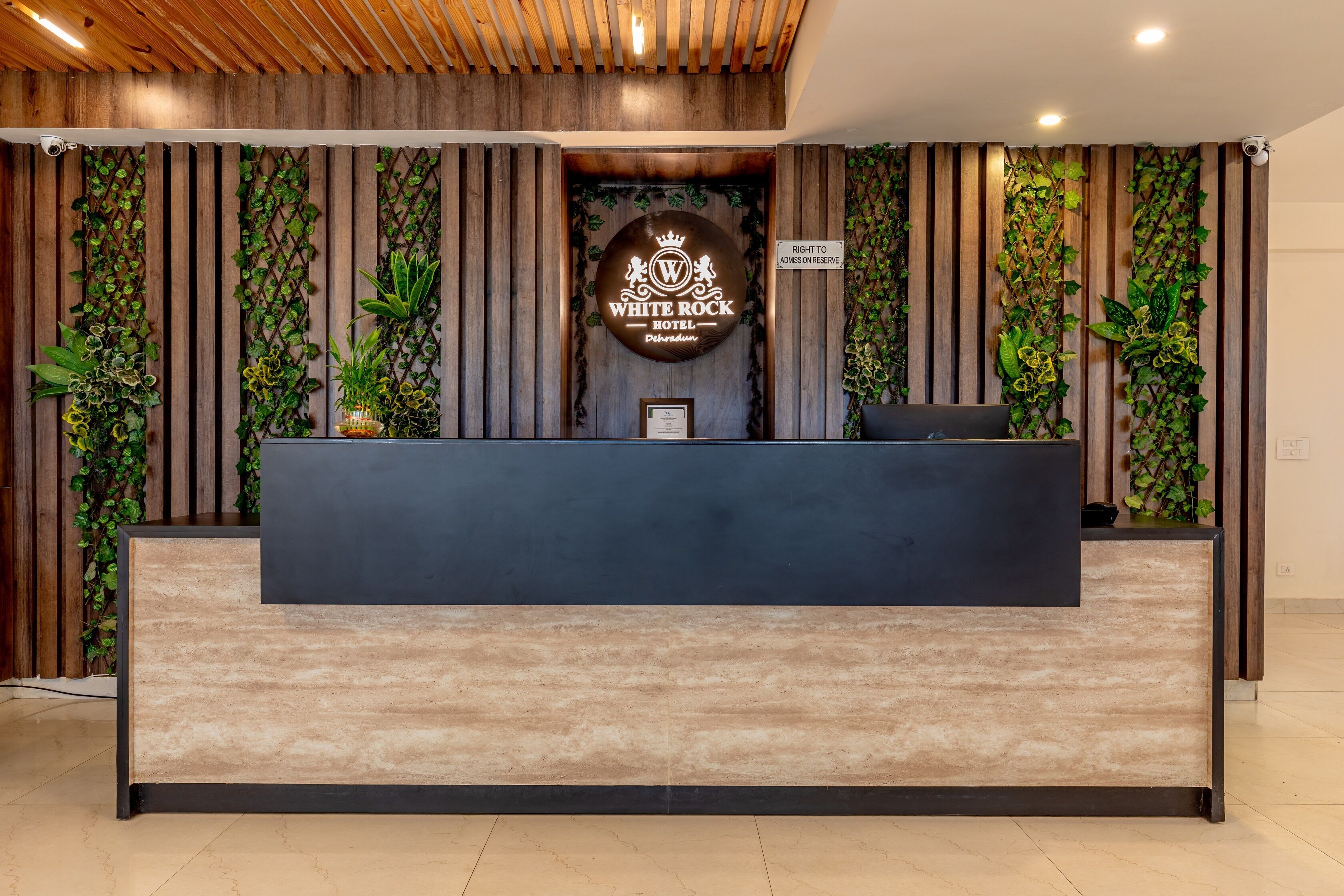 Un comptoir d’accueil orné d’un logo, avec des lambris en bois et des plantes vertes.