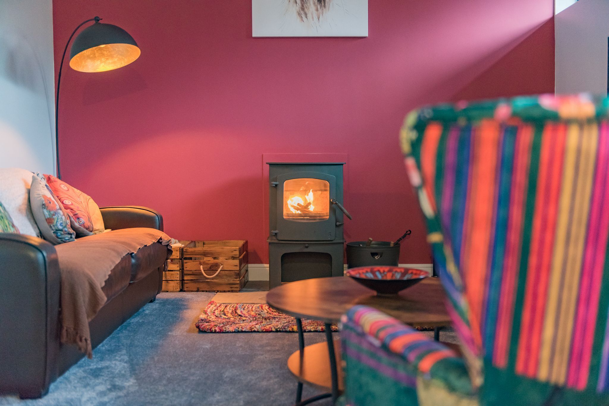 A cozy living room with a sofa, a small table, a colorful chair, a fireplace, and a lamp.