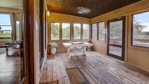 A sunroom with a wooden deck, large windows, and a table with chairs. - Sandy Feet Retreat on LBJ - Pool, Hot Tub, Kayaks (Kingsland)