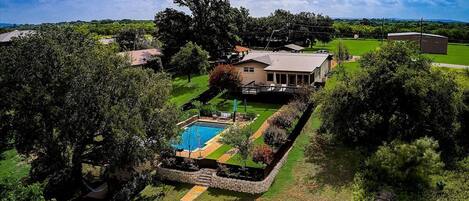 A residential property with a swimming pool, a large house, and surrounding greenery.