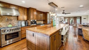 A modern kitchen with wooden cabinets, a large island, stainless steel appliances, and a dining area with leather seating. - Sandy Feet Retreat on LBJ - Pool, Hot Tub, Kayaks (Kingsland)