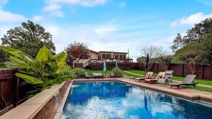 A swimming pool with a wooden deck, lounge chairs, and a house in the background. - Sandy Feet Retreat on LBJ - Pool, Hot Tub, Kayaks (Kingsland)