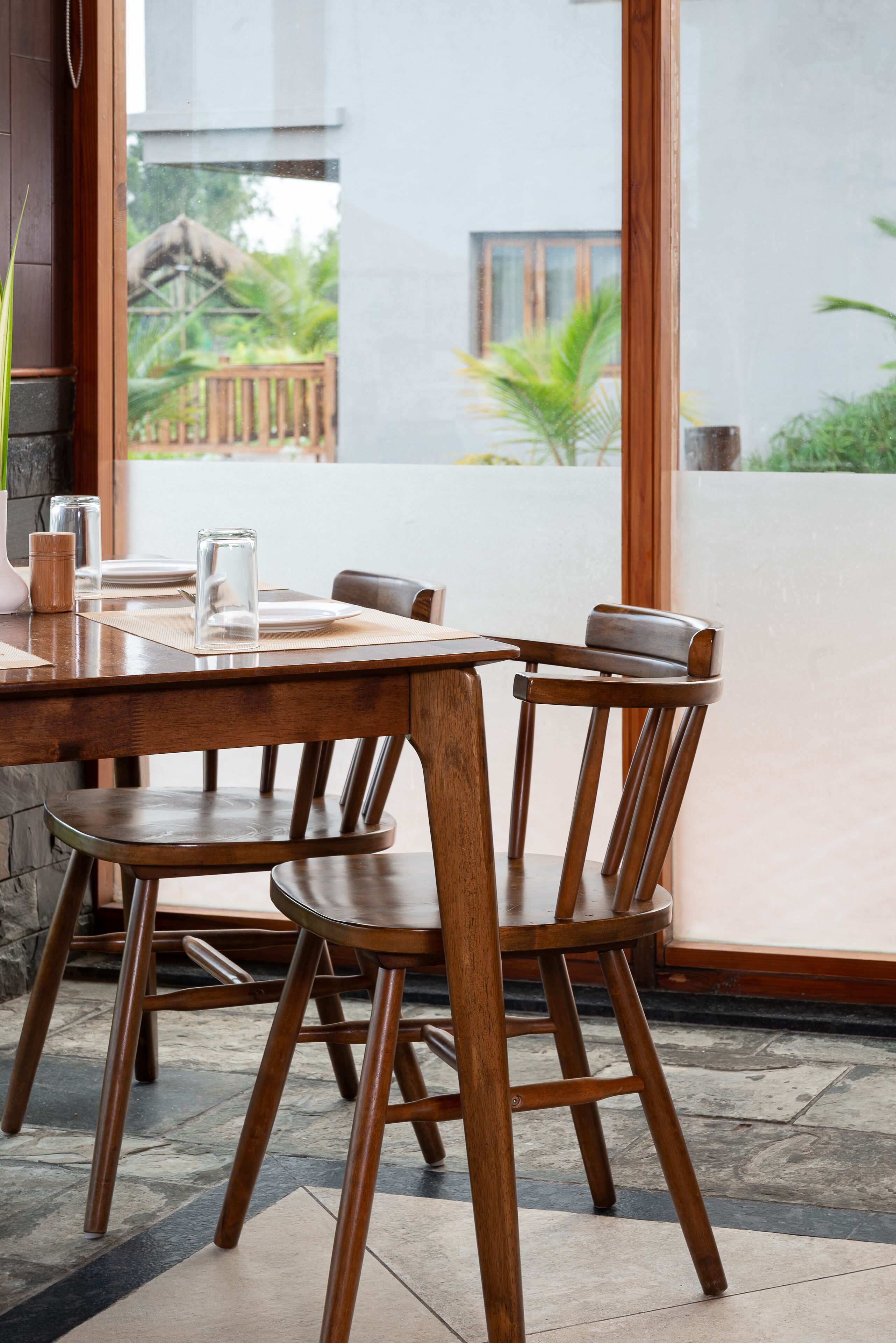 A wooden dining table with chairs, a glass candle holder, and a placemat.