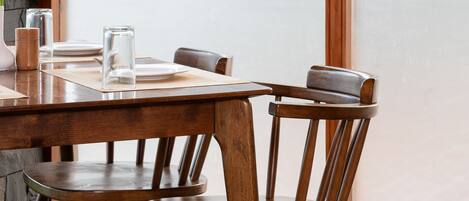 A wooden dining table with chairs, a glass candle holder, and a placemat.