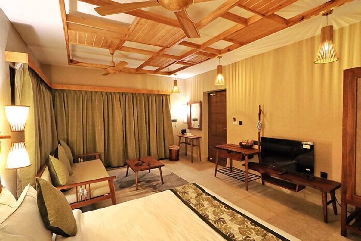 A hotel room with a bed, a TV, a desk, and a chair. There is a window with curtains and a ceiling fan.
