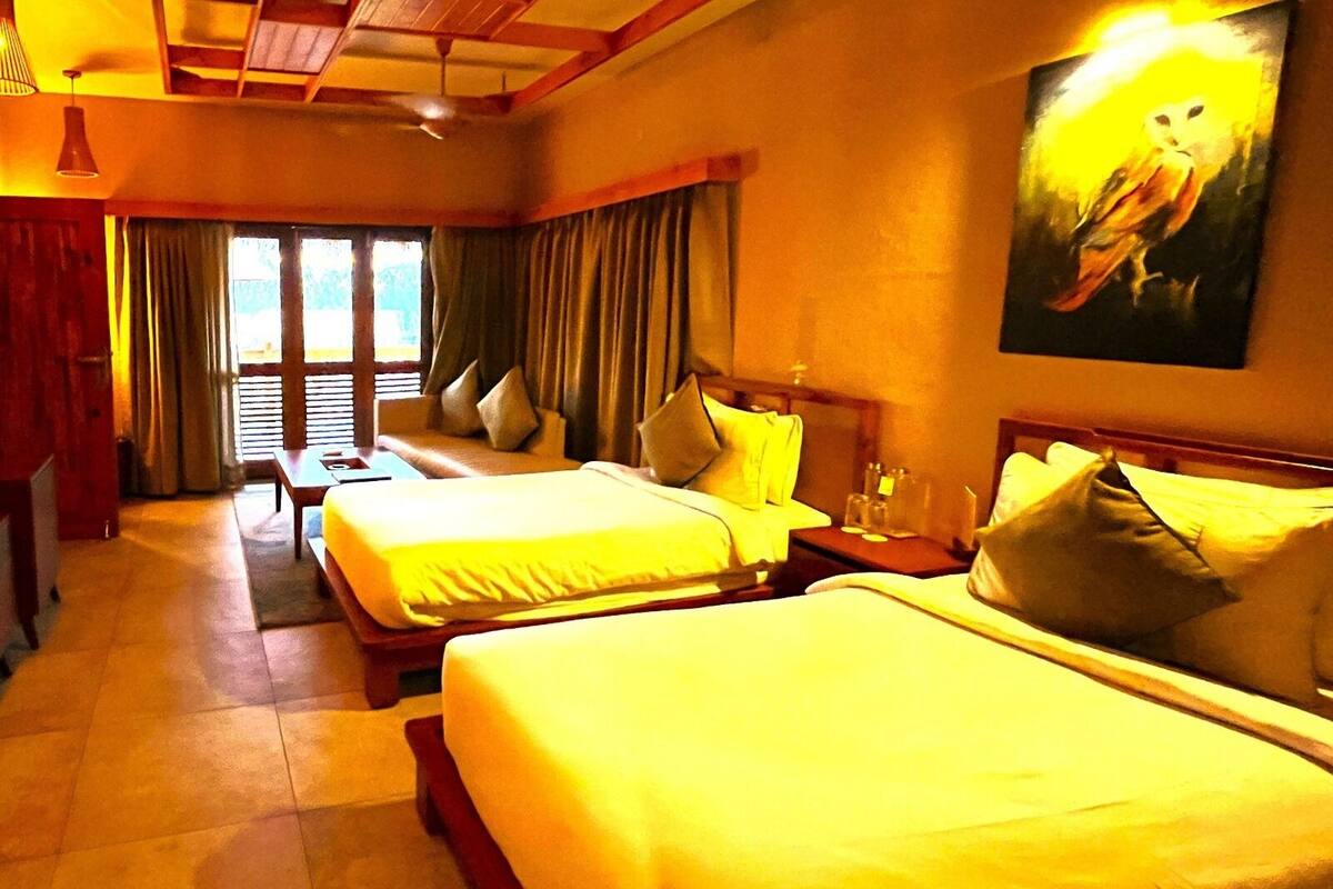 A hotel room with two beds, a wooden headboard, a nightstand, a painting of an owl, and a window with curtains.